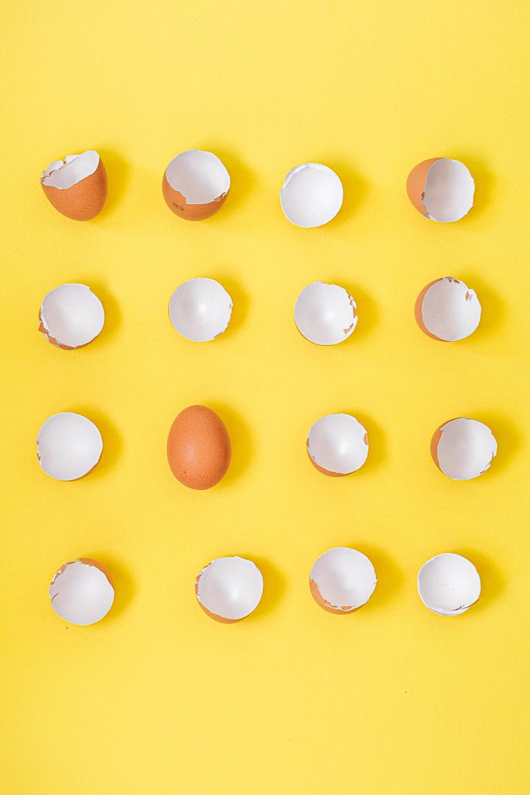 Pattern of whole and cracked brown eggshells on a vibrant yellow backdrop.